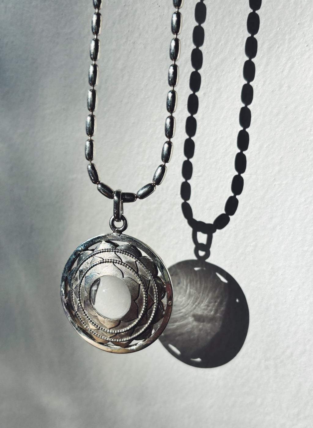 Sterling silver pendant with clear quartz crystal and sacred geometry design casting a shadow on white background