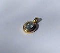 A close-up top-down view of a single, oval faceted pale blue aquamarine gemstone meticulously set within a simple, polished brass bezel on a white background. The pendant features a single brass loop for a chain