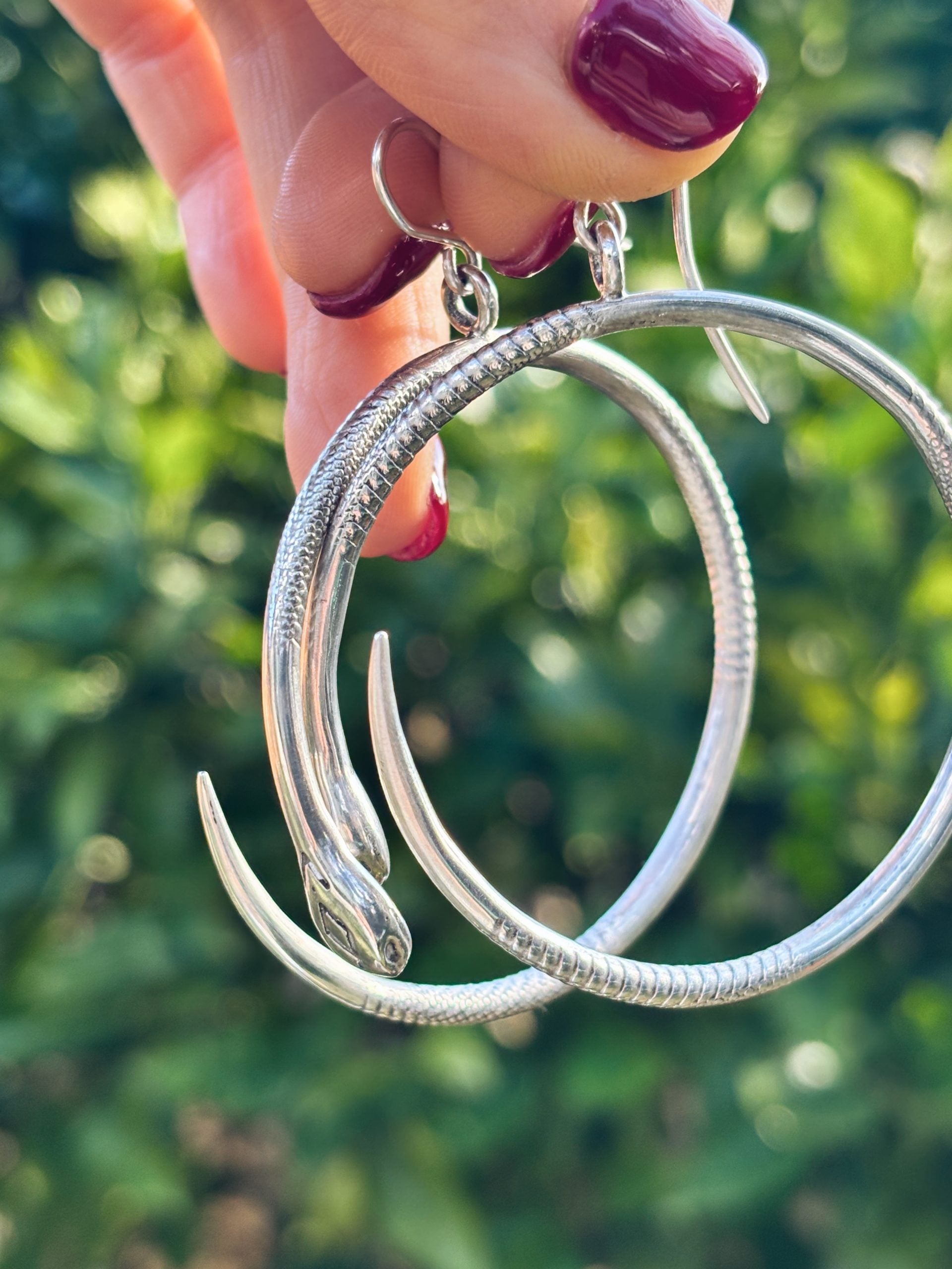 Holding the silver snake earrings in my hand to show the actual size and weight